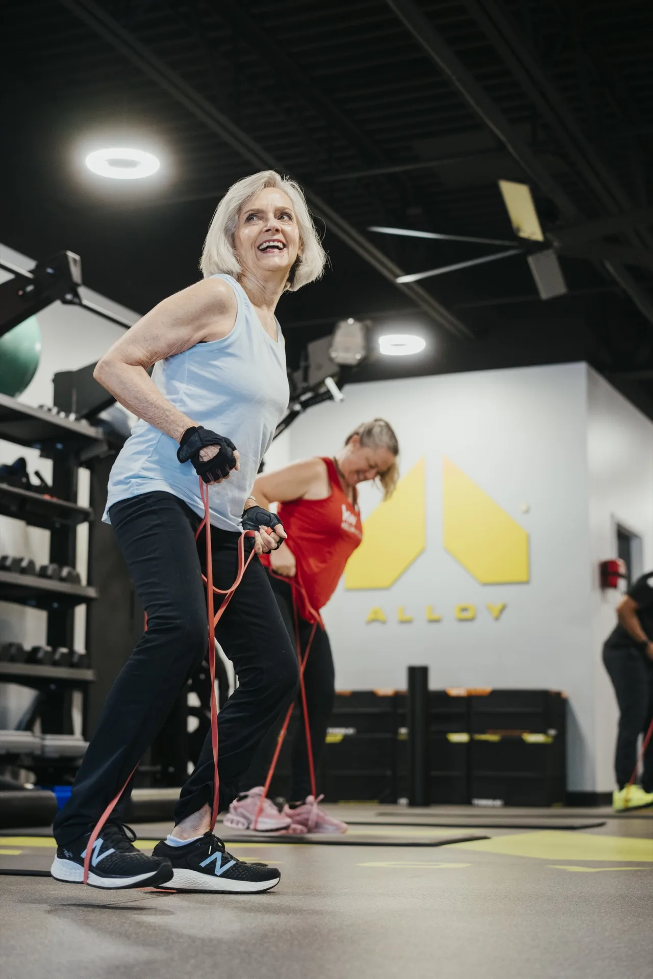 An older member pulls a resistance band while other clients train around her in a small group session