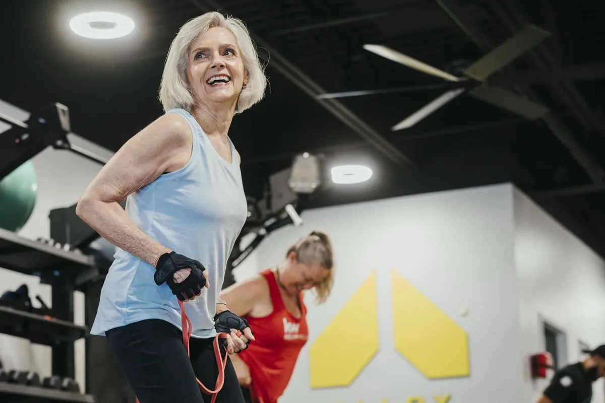A smiling older member works with a resistance band during a small group session at an Alloy studio